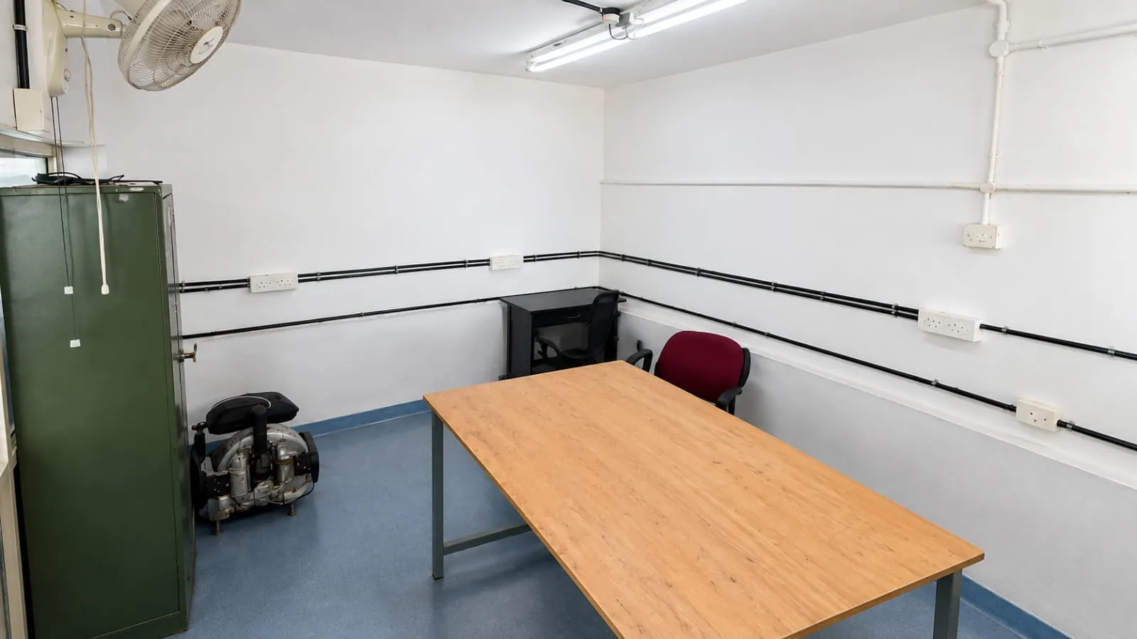 Cabin 4 at TBI MESCE: a long wooden table, a red office chair, a computer desk and power sockets along white walls